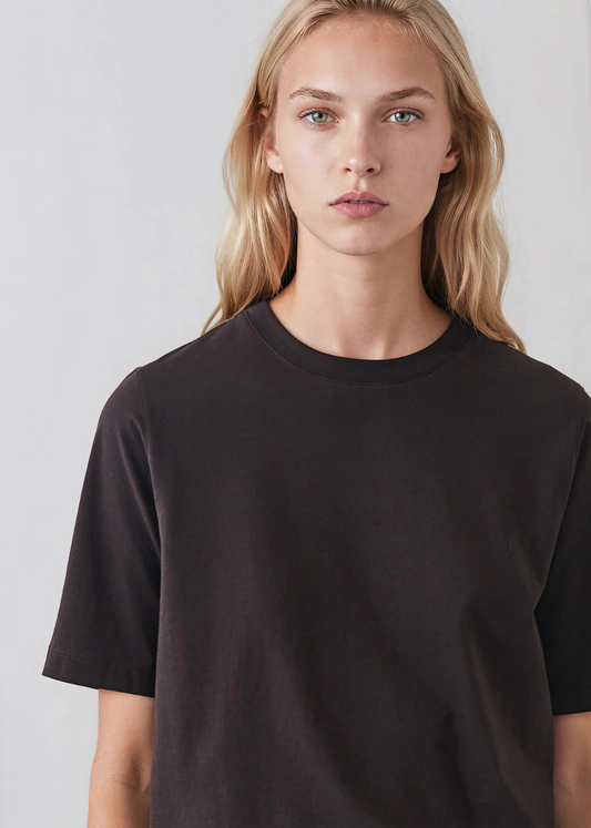 A blonde woman wearing a plain black short-sleeve crewneck t-shirt, photographed against a light gray studio background.